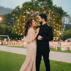 An elegant portrait from an evening reception. The couple poses against a backdrop of trees adorned with fairy lights, creating a romantic scene.