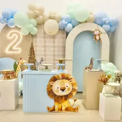 A soft and modern take on a jungle theme for a second birthday. The decor uses a pastel blue and beige color palette with cute, cartoonish animal props like a lion, giraffe, and zebra.