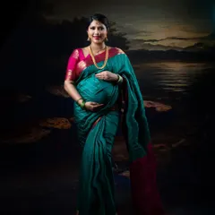 A classic studio portrait of a mother-to-be in a traditional green and pink saree, gently holding her baby bump.
