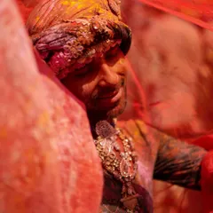 A man celebrating Holi in Nandgaon, his face serene as he is veiled by a translucent red cloth. This is the same powerful portrait also featured in the main carousel, highlighting its significance.