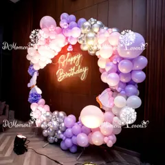 A circular balloon frame in shades of purple, pink, and silver creates a stunning photo opportunity for a 3rd birthday. The design is centered around a bright "Happy Birthday" neon sign, providing a modern and festive focal point.