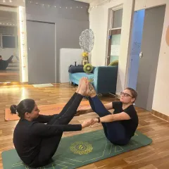 Another pair enjoys the challenge and fun of partner Navasana, smiling as they work together to hold the pose.