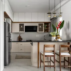 The 'Malhar' kitchen features a mellow monochrome palette with a light blush tone and warm wood accents. The breakfast bar provides a casual spot for meals, connecting the kitchen to the dining space.