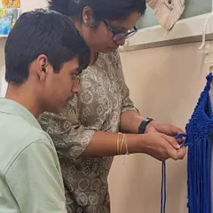 I believe in gentle, one-on-one guidance. Here, I'm helping a student with a macrame knot, ensuring he feels supported and confident as he learns this new skill. This adaptive instruction is at the heart of our special needs art program.