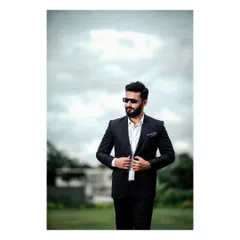 A classic, confident shot for a men's formal wear portfolio. The outdoor setting with a cloudy sky adds a dramatic, sophisticated mood to this image of a man in a black suit.