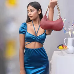 A full-length shot of a model holding a red Sarjaa handbag. This studio image focuses on the relationship between the accessory and the complete outfit, set against a soft, neutral background.