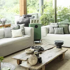 Another view of the sunroom, highlighting the comfortable sofas and the connection to the lush greenery outside. The design prioritizes natural light and an experiential link to the outdoors.