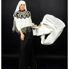 Motion and fabric are captured in this dynamic shot. The model's pose, combined with the flowing white fabric of the hijab, creates a sense of movement and grace against a stark black background, highlighting the unique fringed poncho.