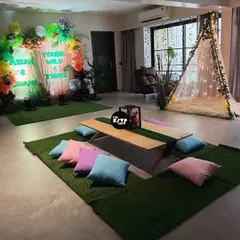 A cozy picnic-style setup for a 'Young, Wild & Three' party, with a low table and colorful cushions on an artificial grass mat.