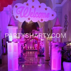 A grand castle entrance designed in pink for a princess party. The setup includes castle turrets and a 'Welcome' sign on a cloud, setting a royal tone from the moment guests arrive.