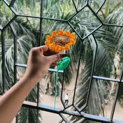 My handmade crochet sunflower held up against the sky. I love how the light catches the texture of the yellow petals and the brown center.