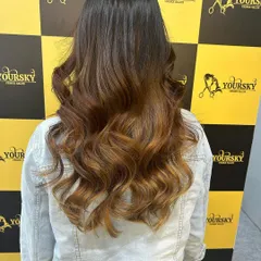 A stunning balayage transformation with warm, caramel tones styled into loose curls against our salon's signature backdrop.