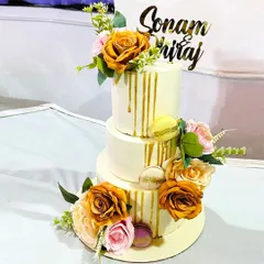 A three-tiered custom wedding cake designed to be the centerpiece of a special day. This elegant cake features a delicate golden drip, macarons, and a cascade of beautiful flowers to match the wedding's theme.