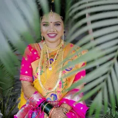 A stunning bridal portrait of a Maharashtrian bride, her smile framed by palm leaves. Her traditional jewelry and vibrant saree are captured in beautiful detail.