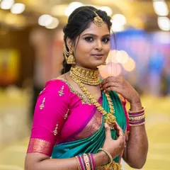 A stunning portrait of our client Asha. She chose a classic gold-finish temple jewellery set, featuring a wide choker and a matching haram, which stands out beautifully against her vibrant teal and pink saree.