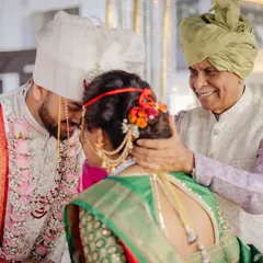 A precious moment between the groom, bride, and her father. This back shot shows the traditional Maharashtrian bridal bun adorned with flowers and a 'kaan vel'.