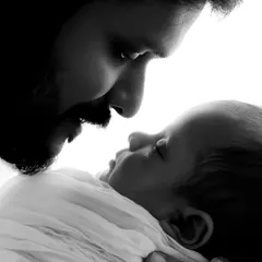 An intimate black and white portrait of a father looking down at his swaddled newborn. The high-contrast lighting creates a dramatic and emotional image that highlights the father-child bond.