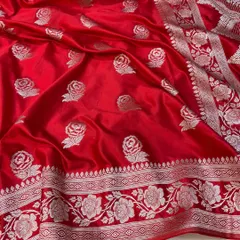 The vibrant red of this Banarasi Mashru silk saree is simply stunning. The silver rose motifs are woven directly into the fabric, creating a luxurious texture and timeless appeal for bridal or festive wear.