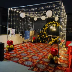 Another perspective of the 'Bride to be' fairy light tent. The black, gold, and red balloon decor adds a touch of glamour to the rustic and romantic lighting setup.