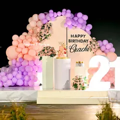 An elegant terrace setup for a 21st birthday. The stage features a pastel balloon arrangement, floral accents, a custom backdrop, and large marquee numbers, creating a stunning focal point for the celebration.