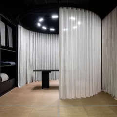 A view of the retail gallery showing the interplay between the dark, austere material palette and the soft, translucent curtains. The design fosters an ambiance of quiet luxury and calm, encouraging slow, mindful discovery.