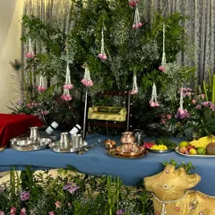 A complete view of our elegant Janmashtami setup. The altar table is draped in blue fabric, with a backdrop of lush green foliage and hanging floral tassels, creating a serene and beautiful space for worship.