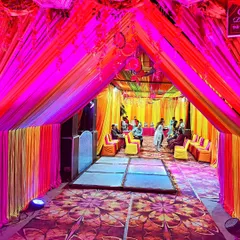 The interior of a Mehendi night tent, illuminated with vibrant pink and yellow lights, featuring a dance floor and guest seating.