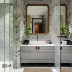 This bathroom showcases our love for material layering. The walls are clad in a striking green and grey marble, paired with a custom fluted vanity from our Koko collection. The wood-framed mirror adds warmth, creating a space that is both bold and balanced.