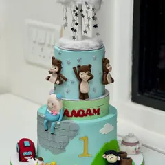 This multi-tiered first birthday cake creates a magical world of adventure. It features hand-crafted monkeys, fluffy clouds, and tiny ducks, with countless details to discover on every level.