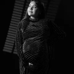 The same artistic lighting style, presented in black and white. This version emphasizes the texture of the gown and the thoughtful expression of the mom-to-be.