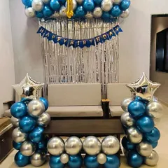 A classic birthday decoration for a home celebration, featuring blue and silver balloon pillars, a shimmer curtain, and a "Happy Birthday" banner.