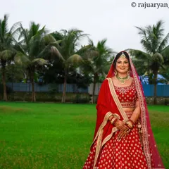 A beautiful wide shot of the bride in her red lehenga, set against a lush green field and palm trees. This type of environmental portrait adds a sense of place and grandeur to the wedding album.