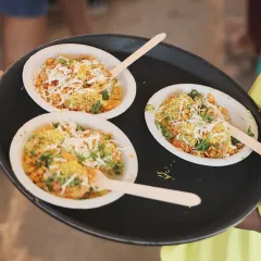 Our chaat is always a crowd-pleaser. This is a close-up of our savory chaat bowls, topped with fresh coriander, sev, and cheese, ready to be served. It's the perfect light and flavorful snack for house parties and events.
