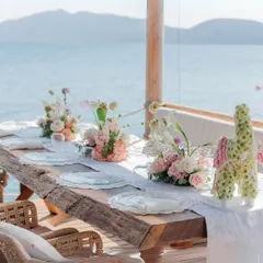An intimate table setting for a seaside lunch in Turkey. The rustic wooden table and delicate florals perfectly complement the natural beauty of the coastline, creating a serene dining experience.