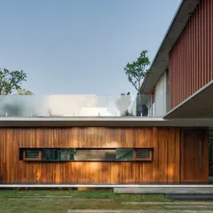 A detail of the Long House facade, where a rich timber-clad wall is punctuated by a sleek, horizontal window. The glass balcony above maintains a sense of lightness.