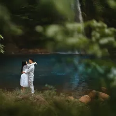 A quiet embrace on the shore of a tranquil blue lake, framed by lush green foliage. This shot highlights our ability to find serene, hidden spots for truly intimate couple portraits.