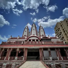 A frontal view of the ISKCON temple in Pune, showing the pathway leading to the entrance under a dramatic cloudy sky.