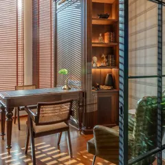 A quiet corner in the office designed as a personal workspace. The combination of a classic wooden desk, a cane-back chair, and natural light filtering through the blinds creates a calm and inspiring atmosphere for focused work.