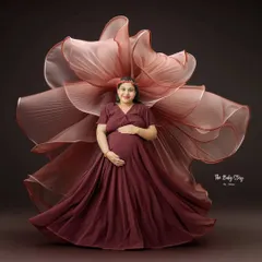 A similar fabric-art technique used with a deep maroon gown. The flowing fabric forms a beautiful floral shape around the mother-to-be, creating a rich and dramatic portrait against a matching backdrop.
