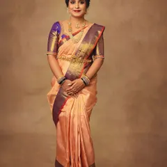 This standing portrait shows the full splendor of the peach and purple silk saree. It's a perfect shot for lookbooks, as it displays the entire outfit, from the drape to the border details.