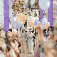 The couple's grand entrance through a crowd of cheering family and friends, all holding balloons, setting a joyful and festive tone for the celebration.