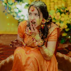 A fun and candid moment as the bride, covered in turmeric, enjoys a sweet treat during her Haldi ceremony.