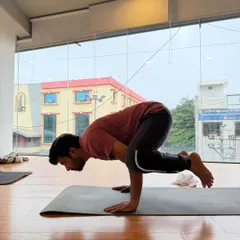 A student demonstrates focus and strength while holding Bakasana (Crow Pose) during a group class.