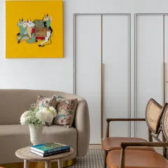 A closer view of the central lounge at Ra Clinic, where clients can unwind before their treatments. The neutral curved sofa, cane chairs, and patterned rug create a textured, comfortable setting. The vibrant yellow artwork, a piece from the client's personal collection, adds a joyful and personal touch to the space.