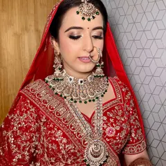 My beautiful bride Vismita in a classic red lehenga. Her makeup features soft golden glittery eyes, a defined liner, and a subtle lip color that complements her green and white kundan jewelry.