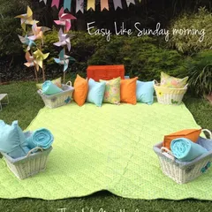 "Easy like Sunday morning." A simple and inviting picnic spot with comfortable blankets and cushions, perfect for a relaxed celebration in the sun.