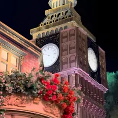 A detailed shot of the Big Ben replica, showcasing the intricate architectural work and the vibrant red flowers adorning the balconies of the adjoining structures, blending London's grandeur with celebratory flair.