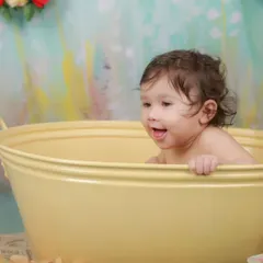 A moment of pure delight during a tub time photoshoot. The colorful, painted backdrop and floral decorations add a whimsical touch to the scene.