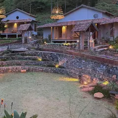 An evening view of the TARA resort, showcasing the terraced landscaping that follows the natural contours of the hill. The warm lighting highlights the natural textures of the stone walls and terracotta roofs.