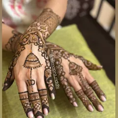 An elegant back hand design featuring a hanging jhumka motif and a personalized initial. This style is a favorite among bridesmaids and family members for its grace.